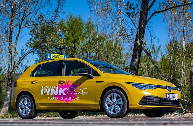 Žuti Volkswagen Golf Auto škole Pink Panter sa strane, sa njihovim znakom i magenta mrljom na vratima.