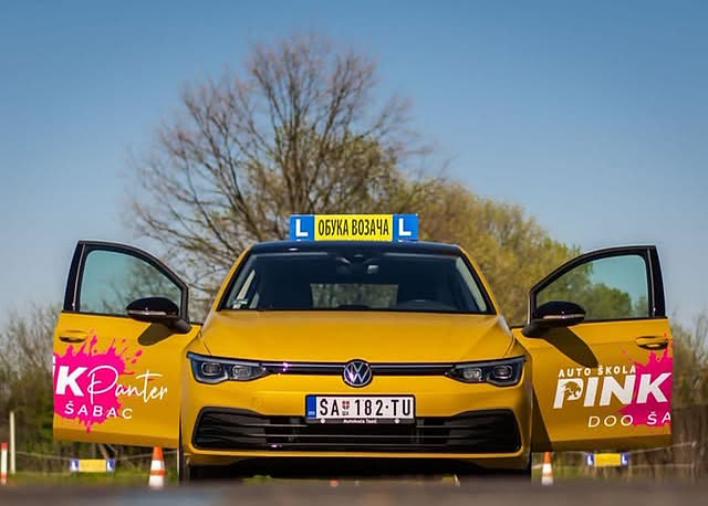 Žuti Volkswagen Golf Auto škole Pink Panter spreda, otvorenih vrata, sa krovnom tablom za obuku.