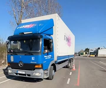 Plavi kamion sa belim sandukom i znakom Pink Pantera na poligonu.