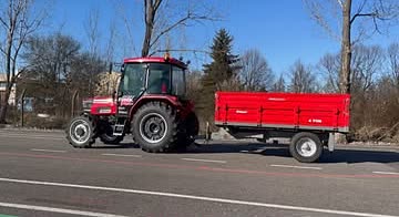 Crveni traktor sa crvenom prikolicom na poligonu.